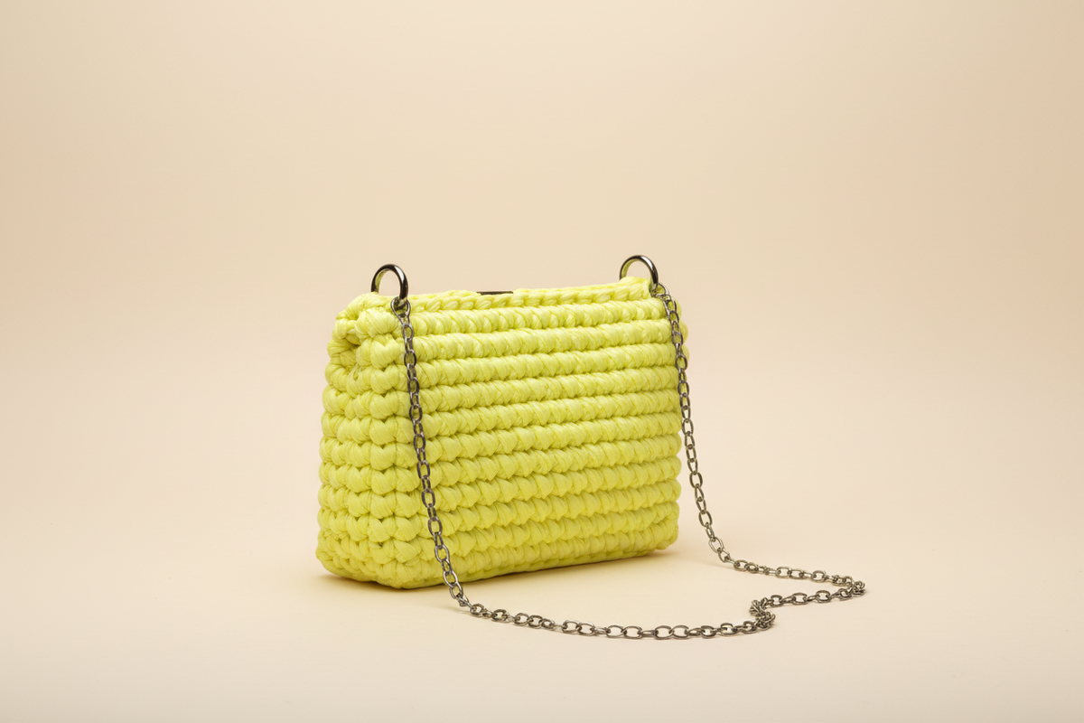 Side three-quarter view of a bright lemon-yellow woven shoulder bag with a chain strap