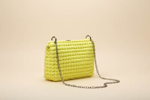 Side three-quarter view of a bright lemon-yellow woven shoulder bag with a chain strap