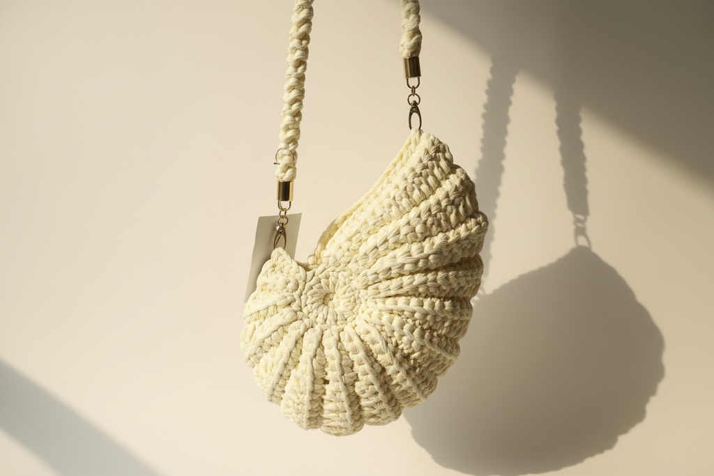 Side three-quarter view of an ivory-white shell-shaped woven shoulder bag