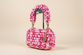 Front three-quarter view of a pink-and-white woven handbag