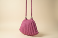 Side three-quarter view of a rose-pink woven shoulder bag with a flared silhouette