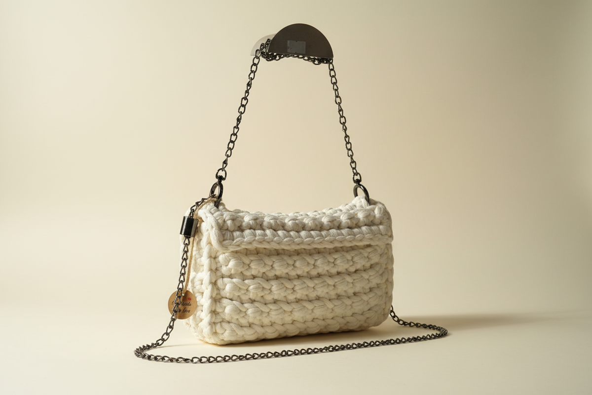 Side three-quarter view of an ivory-white woven flap handbag with a chain strap
