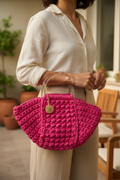Side three-quarter view of a fuchsia shell-shaped woven handbag with clear top handles