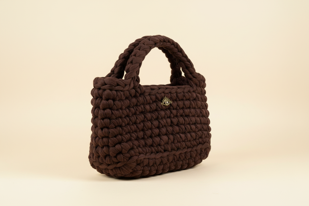 Front three-quarter view of a chocolate-brown woven handbag with braided top handles