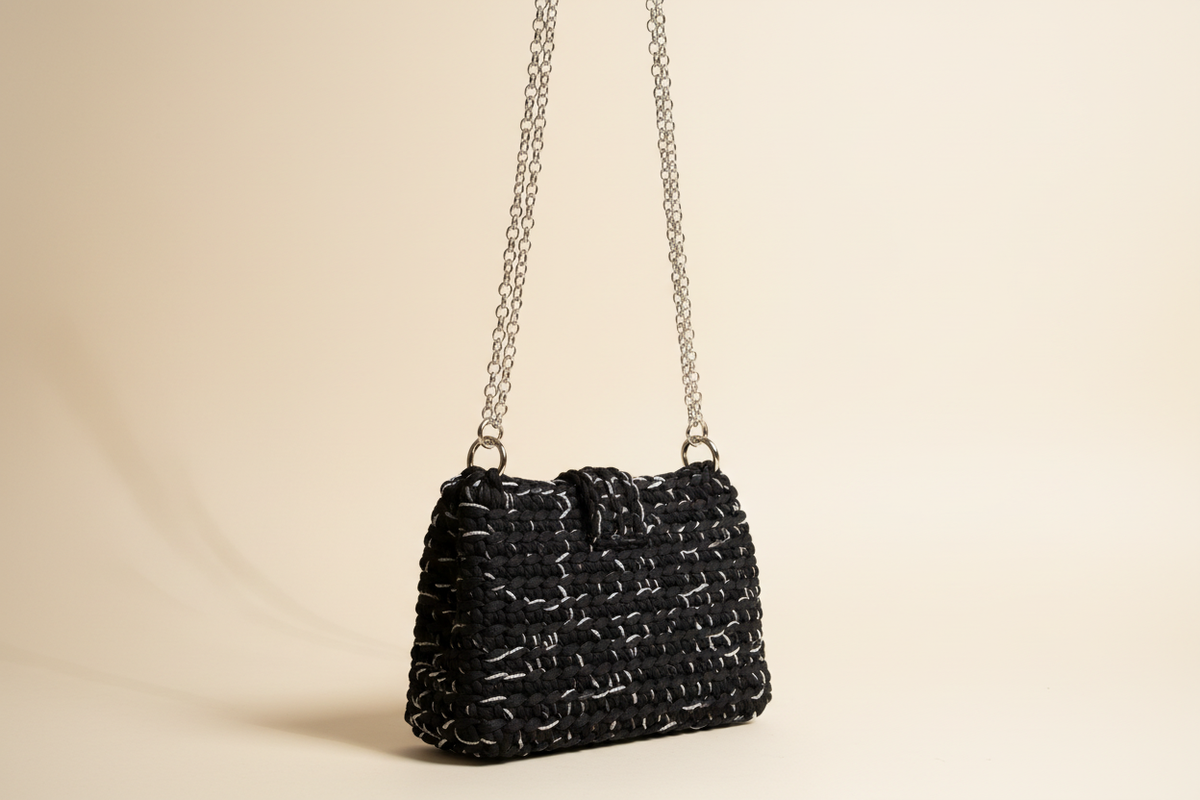 Side three-quarter view of a black woven shoulder bag with a chain strap