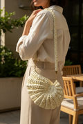 Model wearing an ivory-white shell-shaped woven shoulder bag with a braided strap