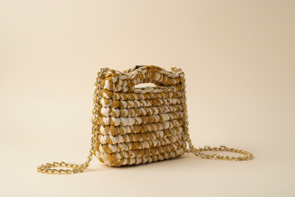 Front three-quarter view of a mustard-and-cream woven shoulder bag with a chain strap
