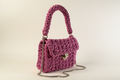 Front-left three-quarter view of a mauve woven shoulder bag with a chain strap and gold-tone clasp