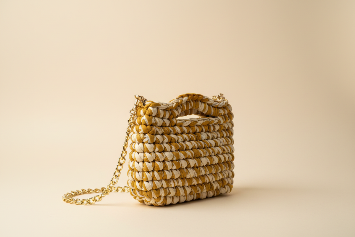 Side three-quarter view of a mustard-and-cream woven shoulder bag with a chain strap