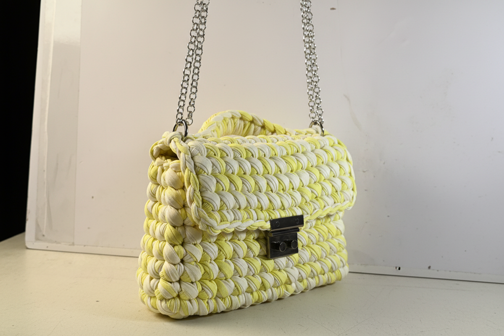 Side three-quarter view of a lime-and-cream woven handbag with a chain strap