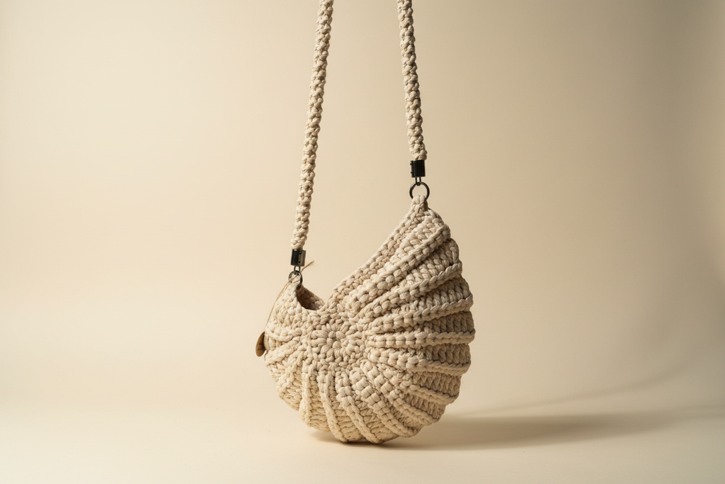 Side three-quarter view of a cream shell-shaped woven shoulder bag