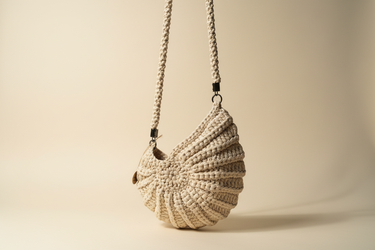 Side three-quarter view of a cream shell-shaped woven shoulder bag