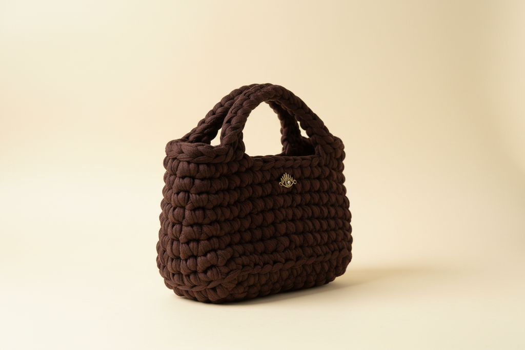 Side three-quarter view of a chocolate-brown woven handbag with braided top handles
