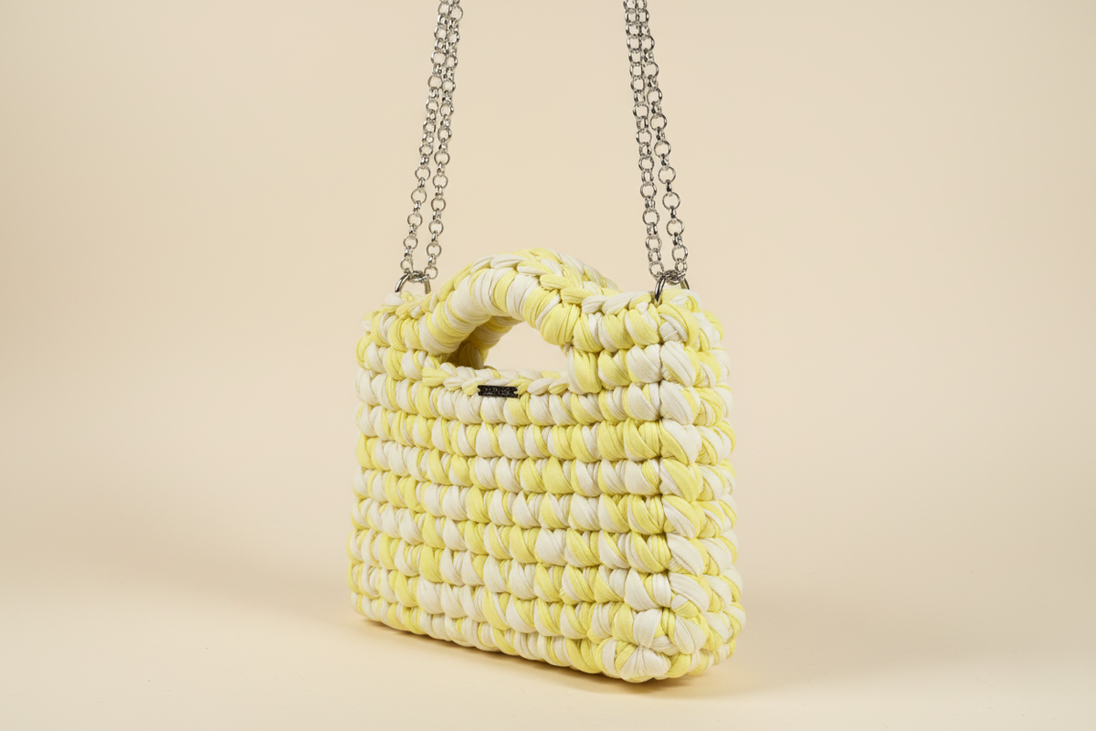 Front three-quarter view of a lime-and-cream woven handbag with a chain strap