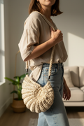 Model wearing a cream shell-shaped woven shoulder bag with a braided strap