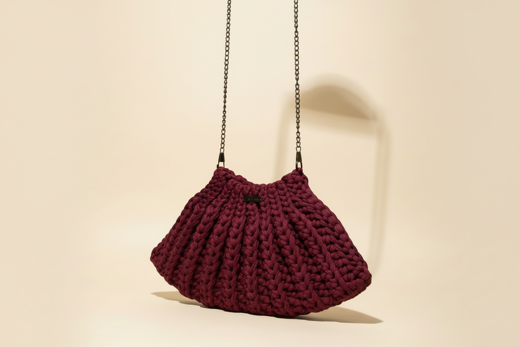Three-quarter view of a burgundy crocheted shoulder bag with a long chain strap