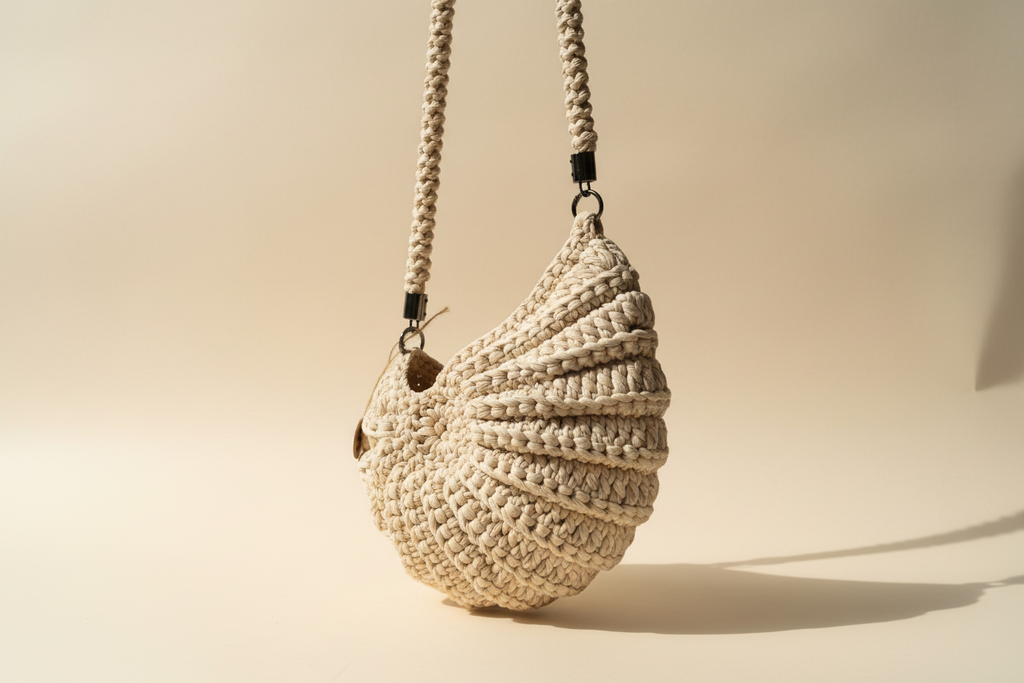 Front three-quarter view of a cream shell-shaped woven shoulder bag