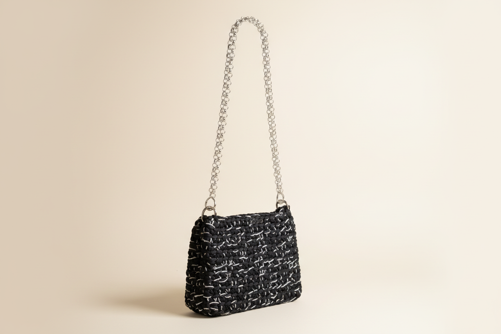 Front three-quarter view of a black woven shoulder bag with a chain strap