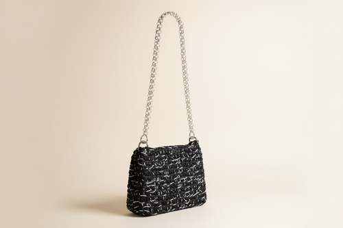 Front three-quarter view of a black woven shoulder bag with a chain strap
