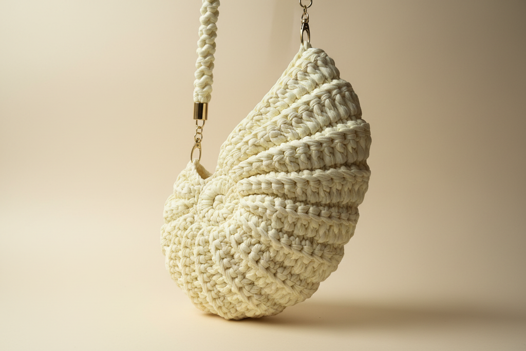 Front three-quarter view of an ivory-white shell-shaped woven shoulder bag