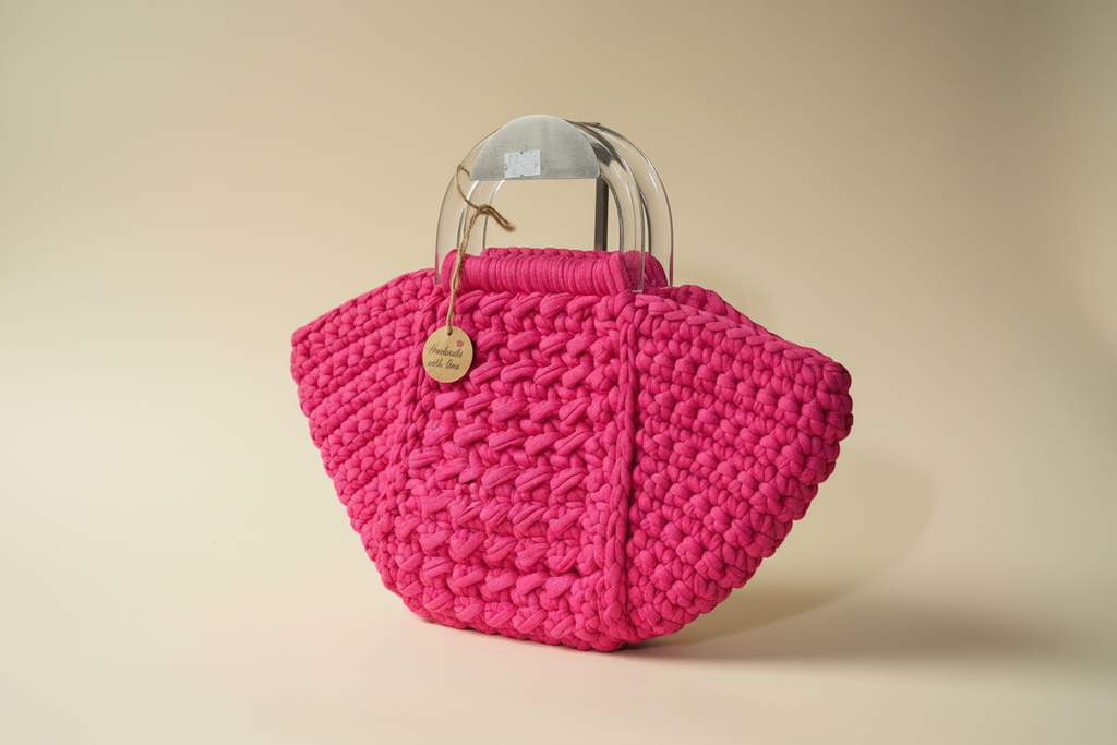 Front three-quarter view of a fuchsia shell-shaped woven handbag with clear top handles